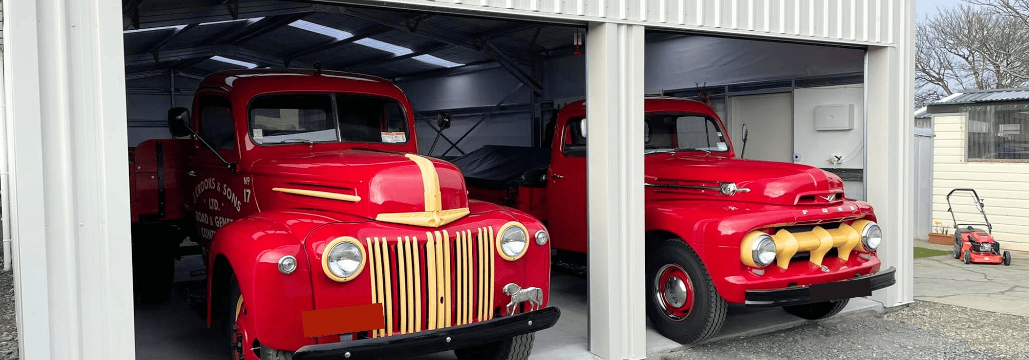 Two classic red trucks in a Wide Span Sheds steel shed